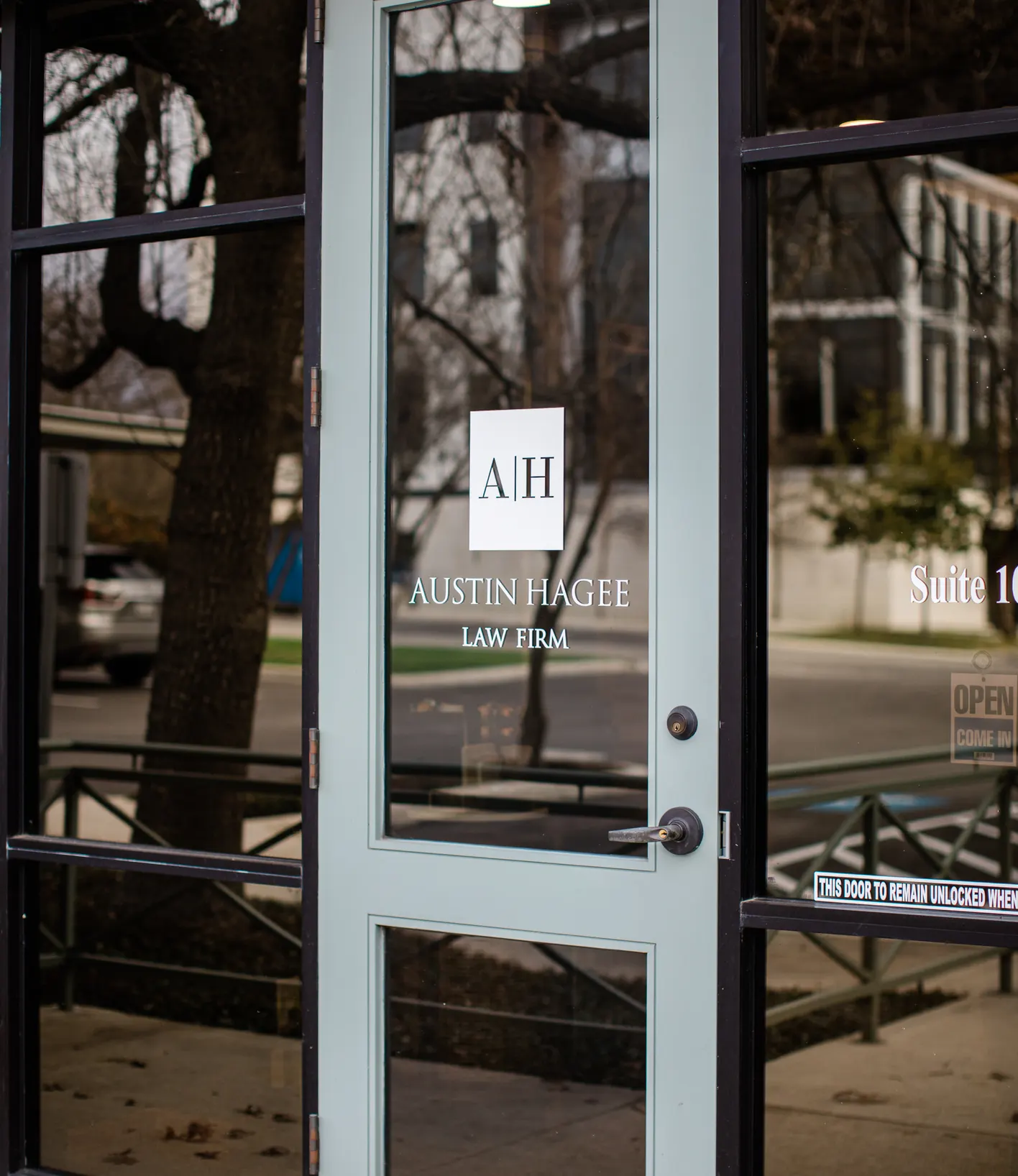 Glass office door etched with the A|H mark and the Austin Hagee Law Firm name at the suite entrance