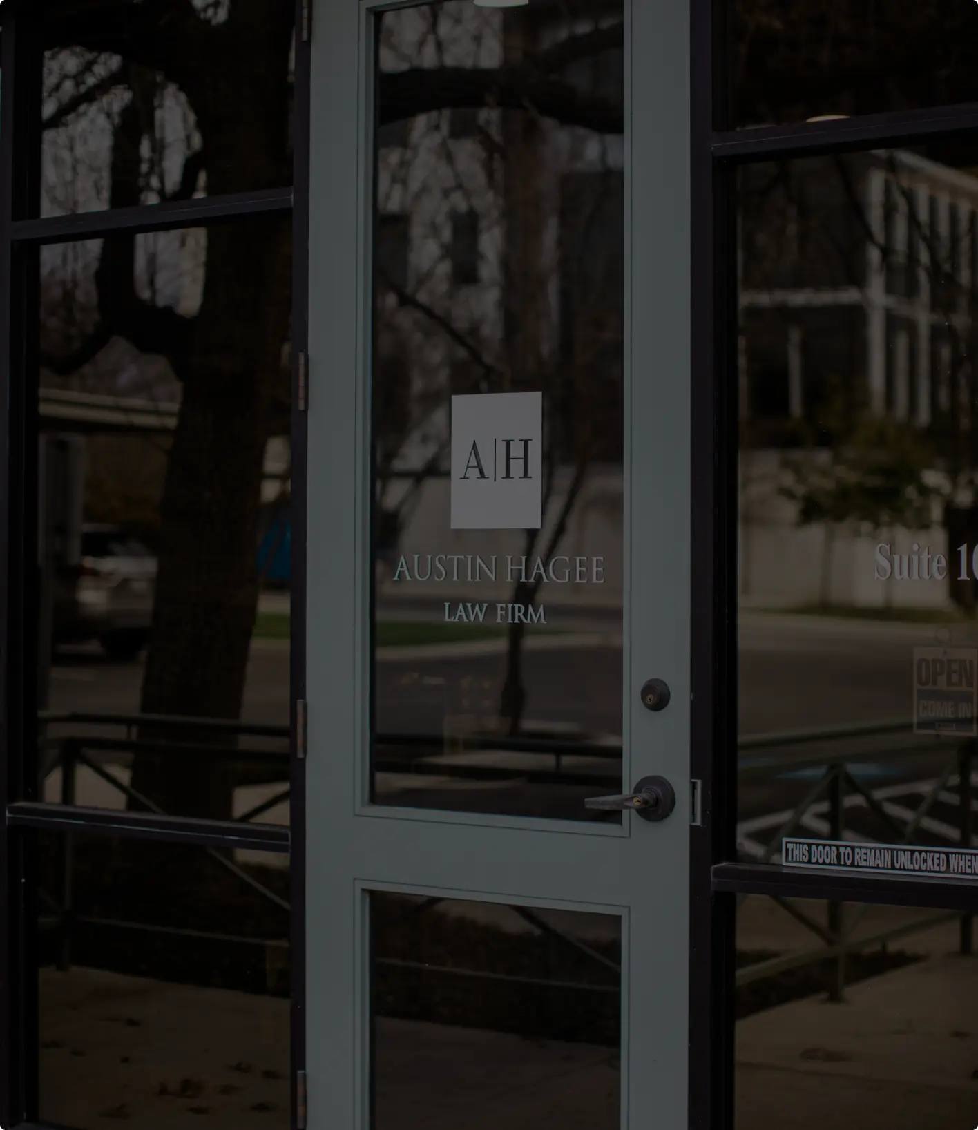Glass office door etched with the A|H mark and the Austin Hagee Law Firm name, seen from the sidewalk