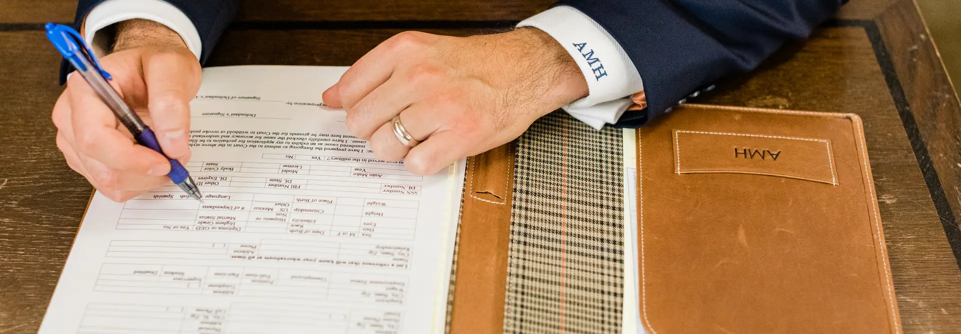 A man in a navy suit filling out a client intake form with a pen at a wooden desk