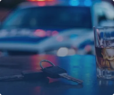 Car keys and a glass of whiskey on a wet street with police car lights blurred behind