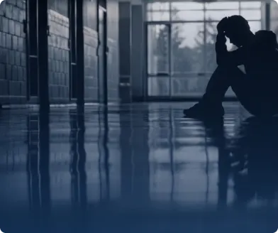 A young person sitting on the floor of a dim corridor with their head in their hands