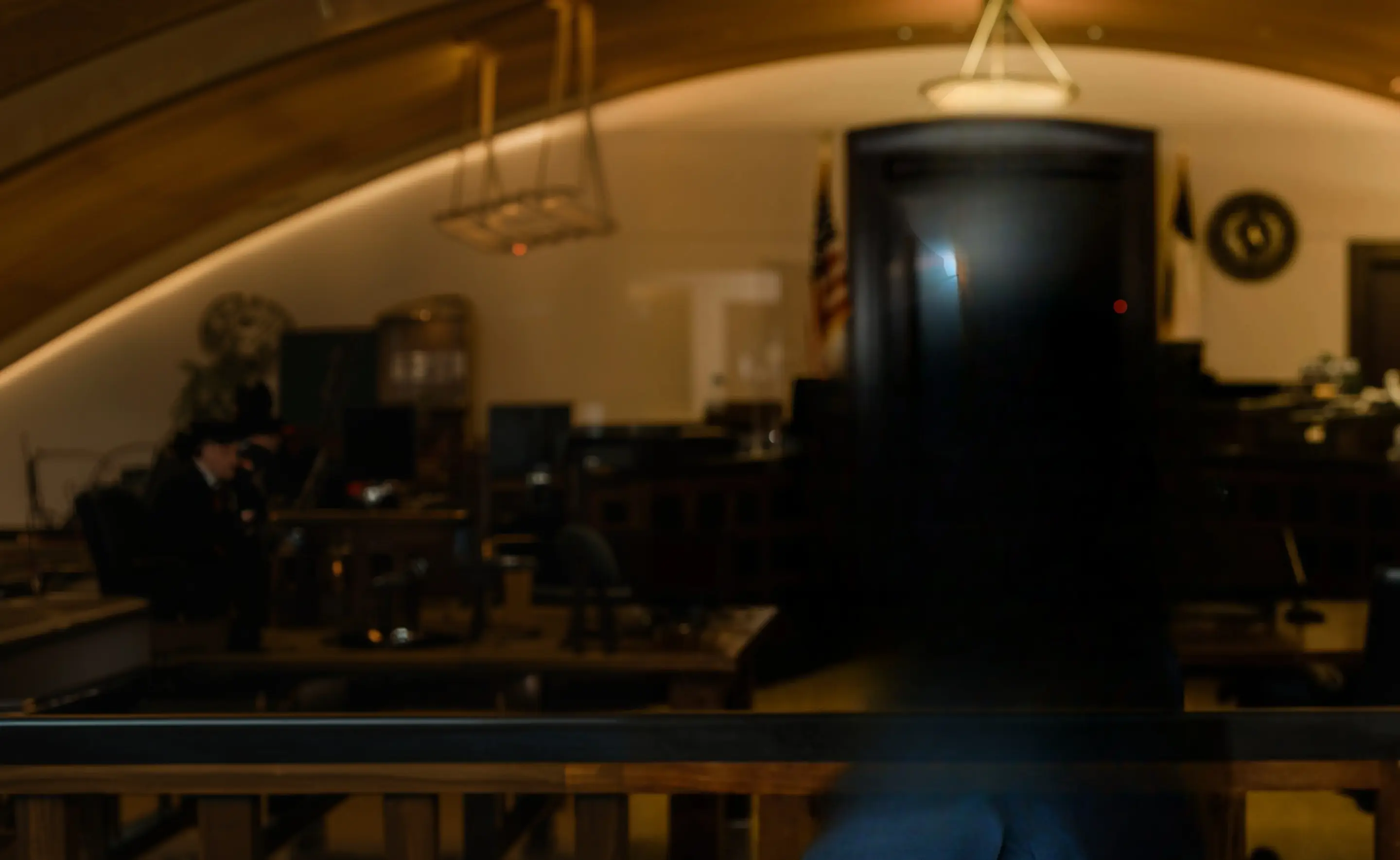 Blurred courtroom interior with wooden benches and rail, hanging lanterns and a flag beside the bench