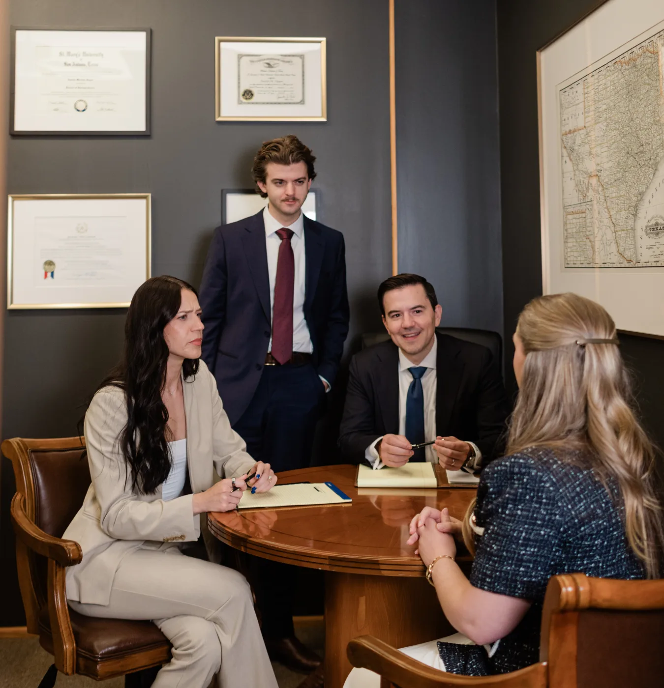 Four of the firm's attorneys meeting at a round table beneath framed diplomas