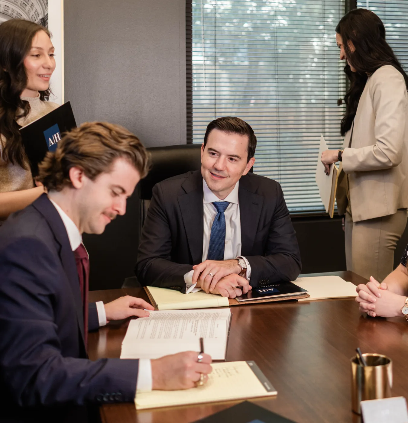 Attorneys at the conference table, one signing a document in the foreground