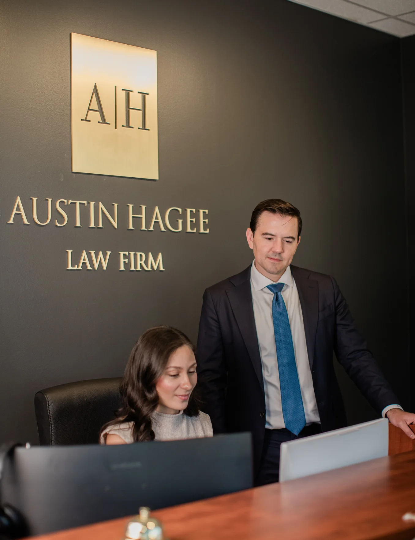 Two members of the firm at the front desk beneath the gold Austin Hagee Law Firm sign